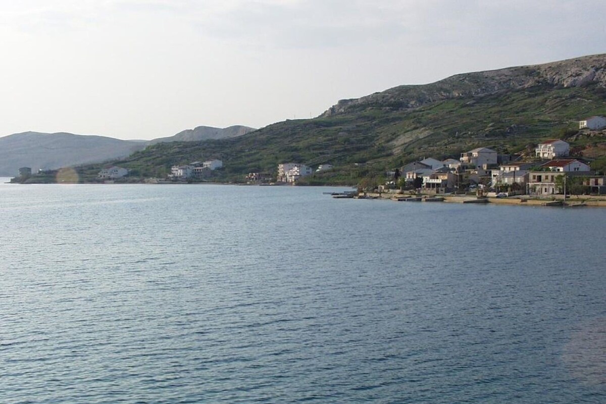 Eine Küstenstadt mit Häusern entlang der Uferlinie, einem ruhigen Meer und Hügeln im Hintergrund.