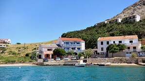 A coastal town with buildings along the waterfront, a clear blue sea, and a hilly backdrop. - Apartments Draga (Novalja)