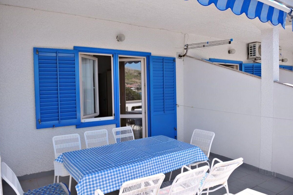 Eine Terrasse mit Tisch und Stühlen, blauen Fensterläden und einer Klimaanlage.