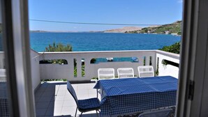 A balcony with a checkered tablecloth, white chairs, and a view of the sea. - Apartments Draga (Novalja)