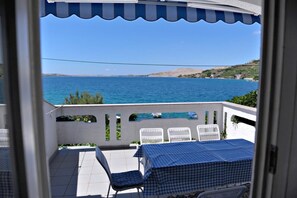 Ein Balkon mit kariertem Tischtuch, weißen Stühlen und Blick aufs Meer.