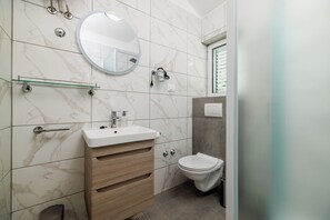 A modern bathroom with a marble backsplash, a round mirror, a white sink, and a toilet. - Apartment Ren (Rab)