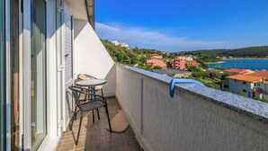 Ein Balkon mit Tisch und Stühlen, mit Blick auf eine Küstenstadt mit Häusern und blauem Himmel.