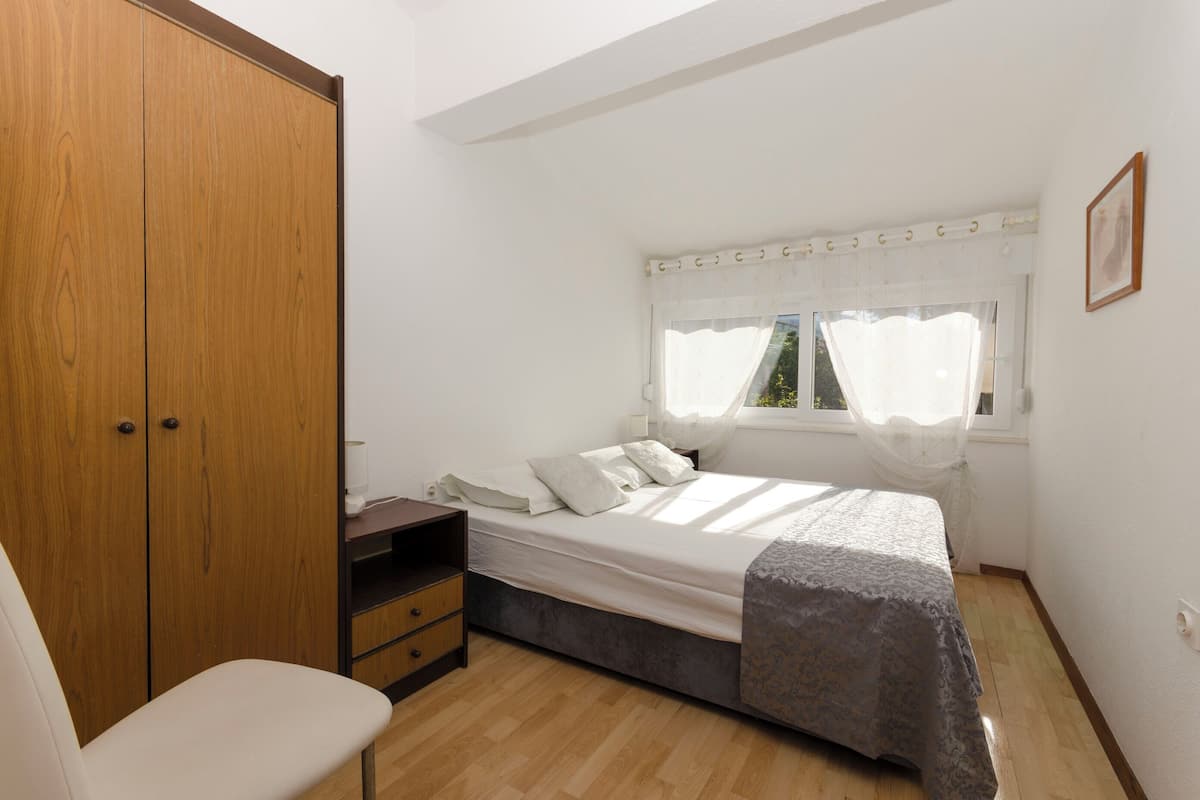 Ein Schlafzimmer mit Bett, Stuhl, Kleiderschrank und einem Fenster mit Vorhängen.