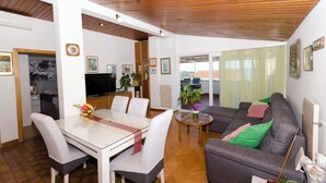 A modern living room with a dining area, wooden ceiling, and a large window with curtains. - Apartments Jadro (Makarska)
