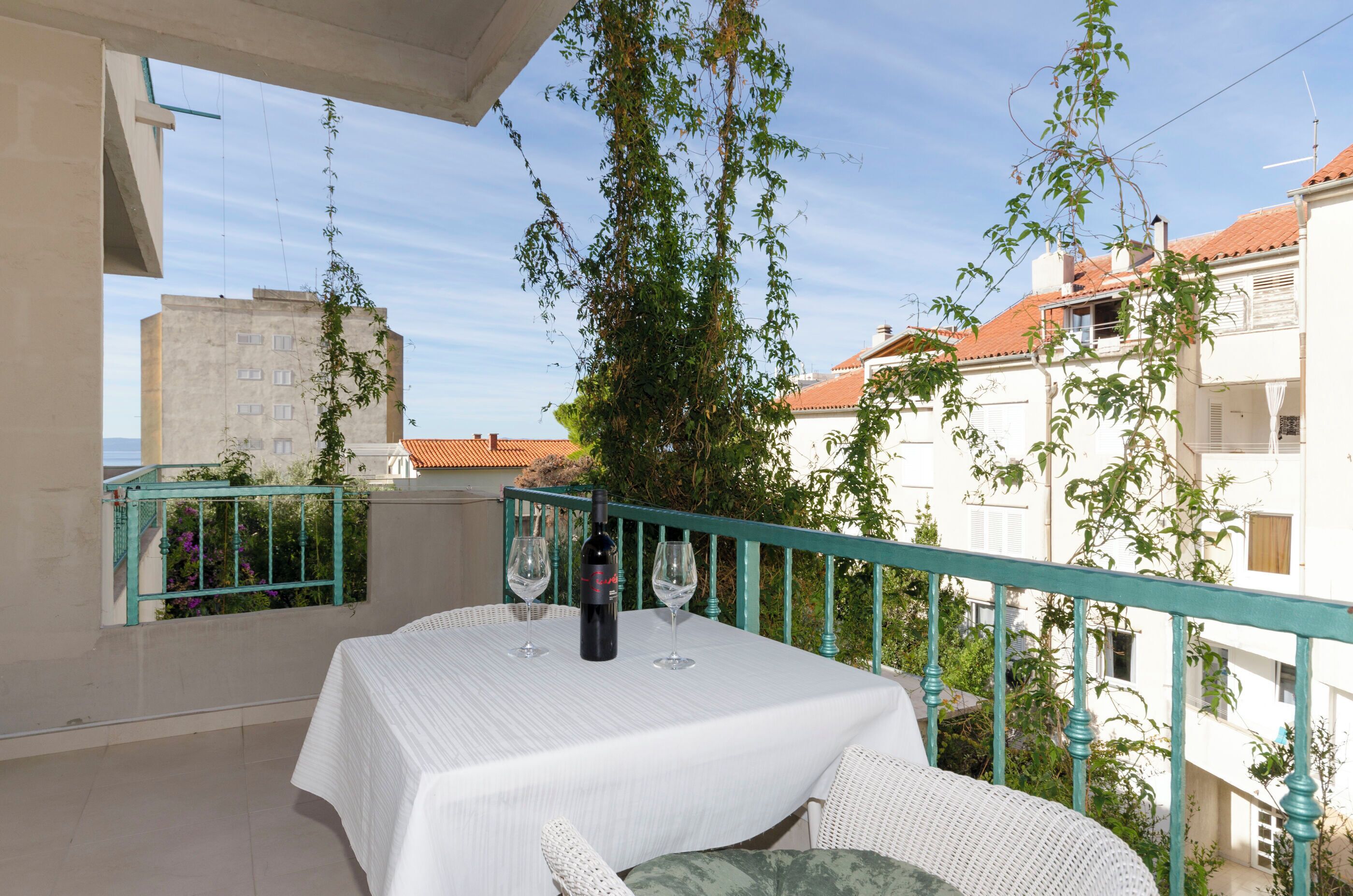 Un balcon avec une table dressée pour deux personnes, deux verres à vin et une bouteille de vin.