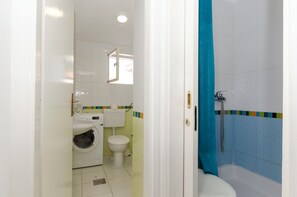 A bathroom with a washing machine, toilet, and shower area. - Apartments Jadro (Makarska)