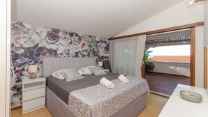 A bedroom with a large bed, a nightstand, a bedside table, and a view of the outside through a sliding door. - Apartments Jadro (Makarska)