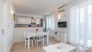 Een moderne, goed verlichte woonkamer met een eethoek, een keuken en een aan de muur bevestigde televisie.