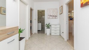 Een gang met een klok, een potplant, een schilderij en uitzicht op een badkamer.