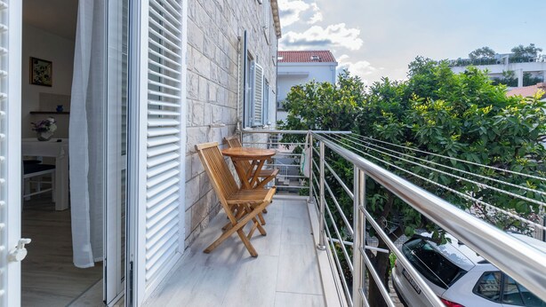 Een balkon met een tafel en stoelen, een nabijgelegen geparkeerde auto en uitzicht op de omliggende gebouwen en begroeiing.