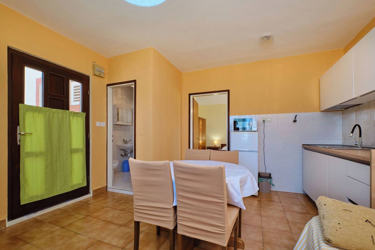 A compact room with a bed, a small dining table, a kitchenette, and a bathroom visible through an open door.