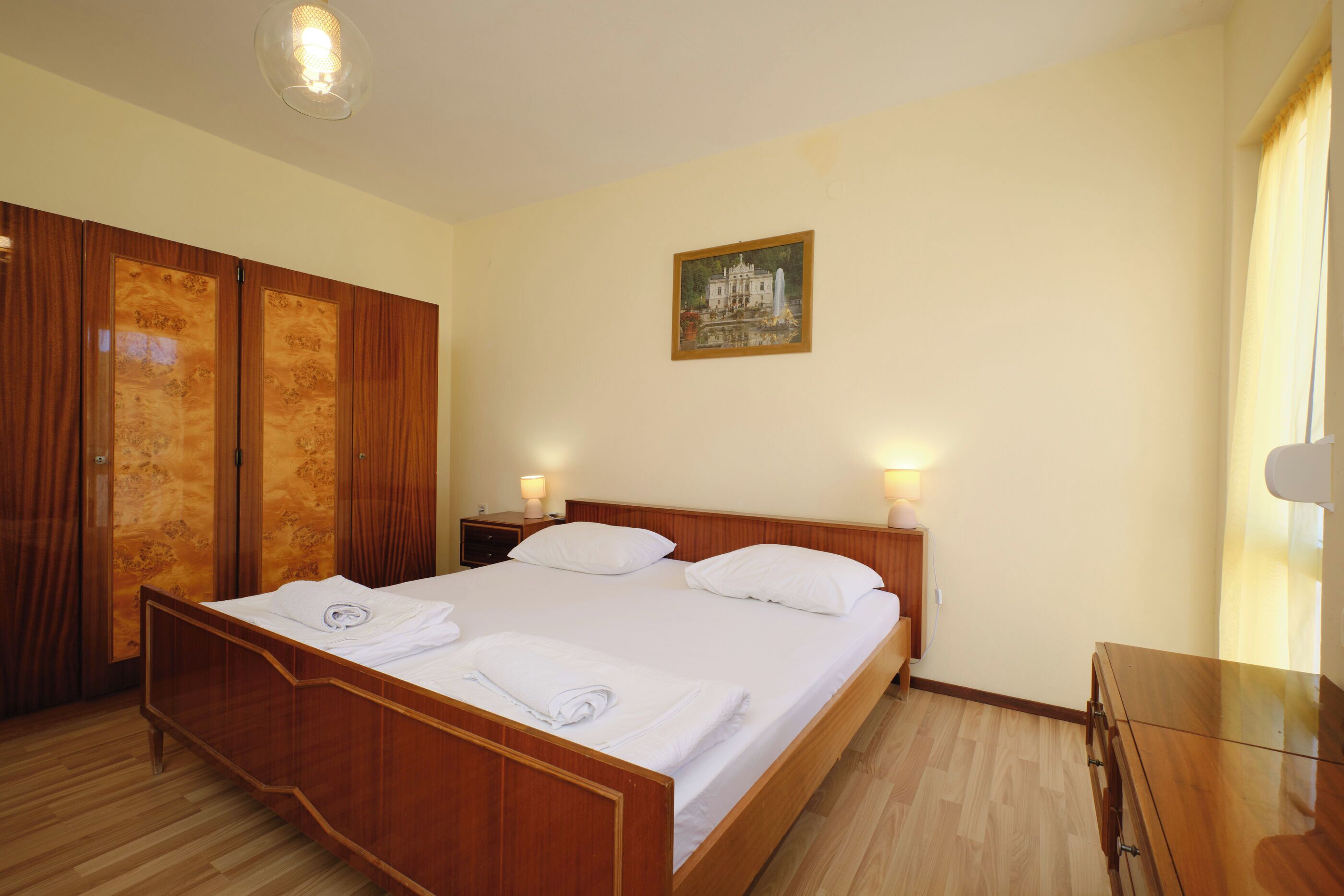 A hotel room with a wooden bed, a nightstand, a wardrobe, and a painting on the wall.