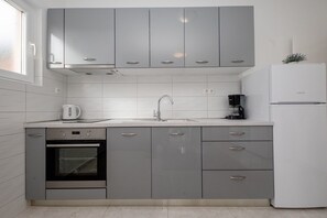 A modern kitchen with grey cabinets, a built-in oven, a sink, and a refrigerator. - Apartments Mar (Rab)