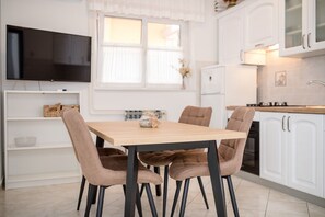 A modern kitchen with white cabinets, a wooden dining table, and four brown chairs. - Apartments Mar (Rab)