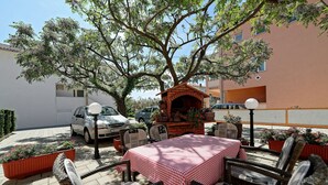 Une terrasse extérieure dotée d’un four à pizza en briques, de meubles en osier et d’une nappe à carreaux rouges et blancs.