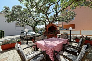 An outdoor seating area with a brick pizza oven, wicker chairs, and a checkered tablecloth. - Apartments Mar (Rab)