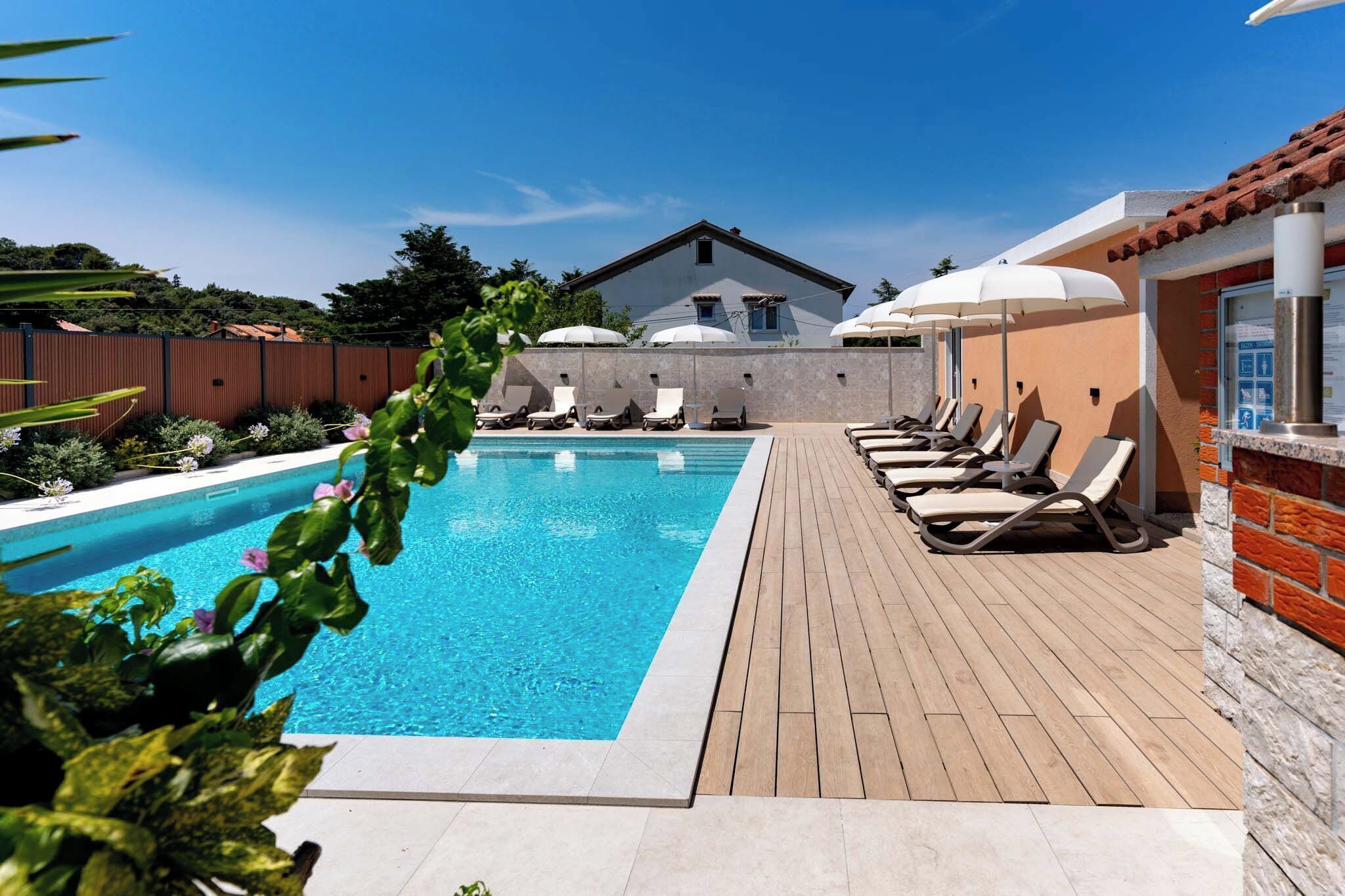 A swimming pool with lounge chairs and umbrellas, surrounded by a wooden deck and a brick wall.