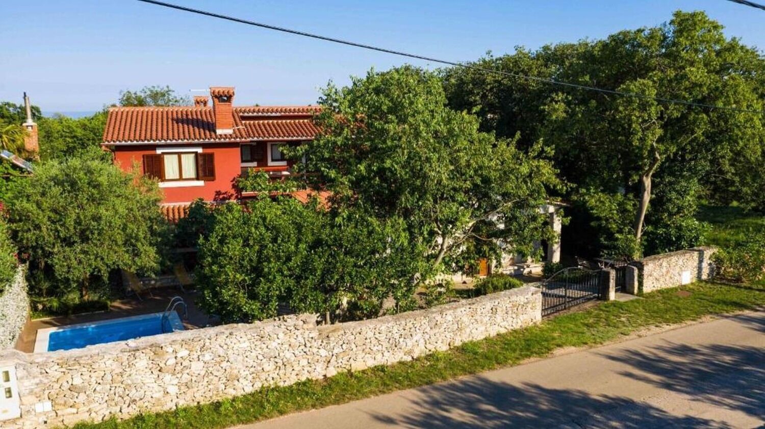 A red villa with a stone wall and a swimming pool.