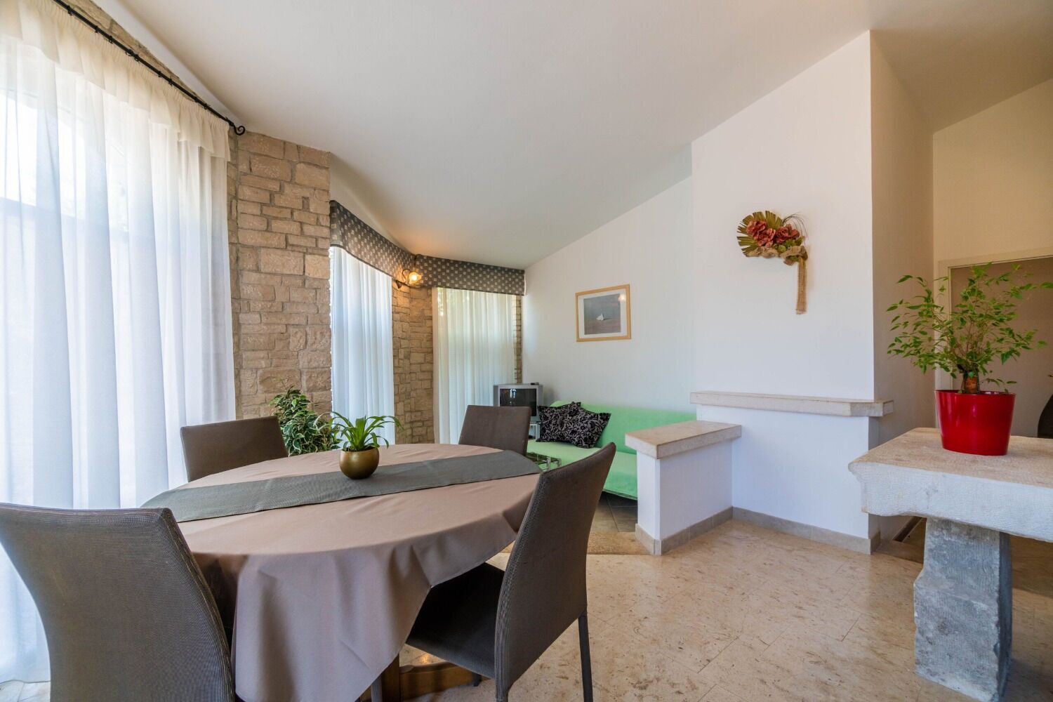 Un coin repas avec une table, des chaises et un canapé vert. On trouve une plante en pot sur la table et une autre sur une table d’appoint.