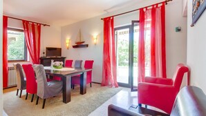 A dining area with a table and chairs, a television, and a view of the outdoors through a sliding glass door. - Apartments Eli (Mali Losinj)