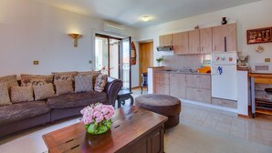 A modern living room with a sofa, a coffee table with flowers, a dining area, and a kitchen with cabinets and appliances. - Apartments Eli (Mali Losinj)
