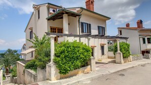 A two-story house with a covered porch, a chimney, and a view of the sea. - Apartments Eli (Mali Losinj)