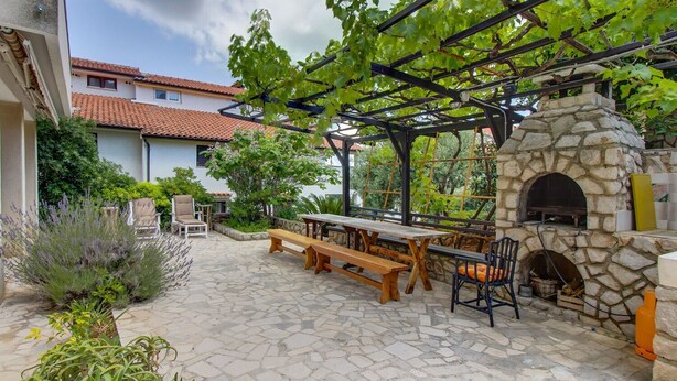 An outdoor patio with stone flooring, a wooden table, benches, and a stone-built pizza oven. - Apartments Eli (Mali Losinj)