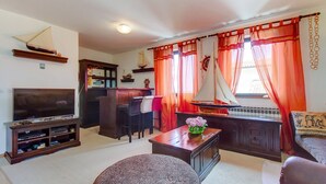 A living room with a television, wooden furniture, a small table with a vase, and red curtains. - Apartments Eli (Mali Losinj)