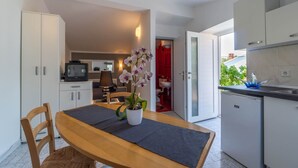 A compact kitchen with white cabinets, a small dining table with a dark placemat, and a potted orchid. - Apartments Perci (Marcana)