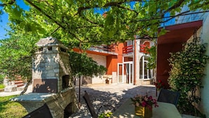 A courtyard with a stone bench, a table with chairs, and a building with red walls and a stone archway. - Apartments Perci (Marcana)