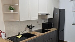 A modern kitchen with white cabinets, a black refrigerator, and a wooden countertop. - Apartment Gianfranko (Opatija)