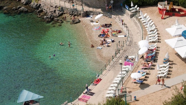 An aerial view of a beach with clear water, sun loungers, umbrellas, and a lifeguard tower. - Apartment Gianfranko (Opatija)
