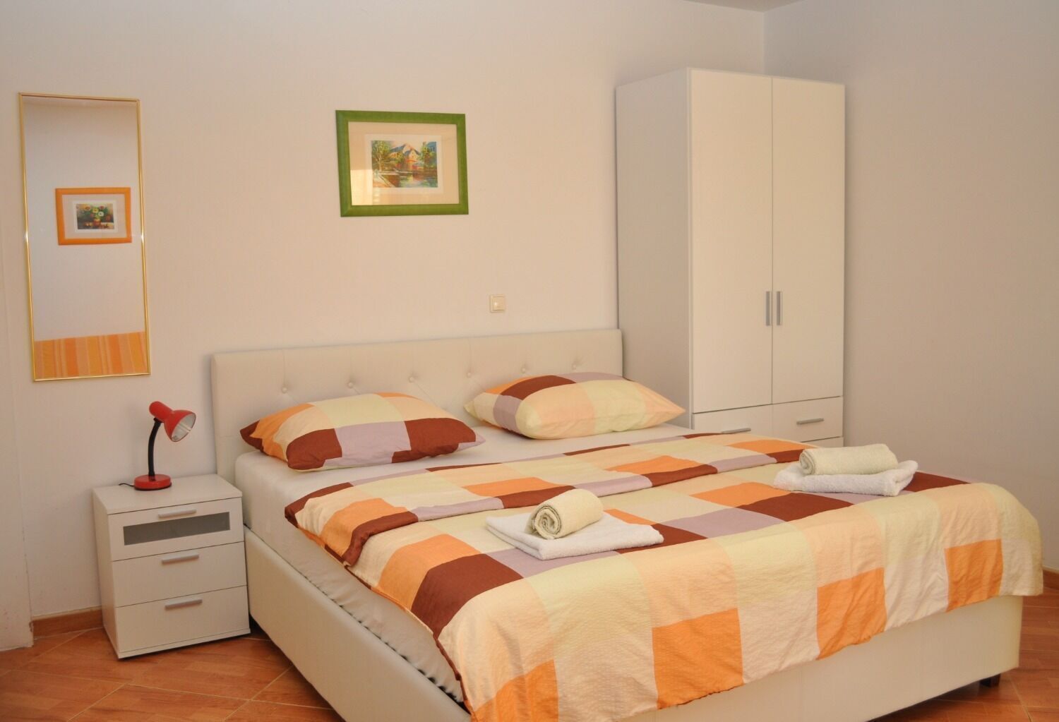 A bedroom with a bed, a nightstand, a wardrobe, and a framed picture on the wall.