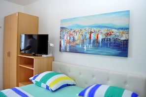 Ein Schlafzimmer mit Bett, Kissen, einem Fernseher auf einem Schrank, einem Bild an der Wand und einem Kleiderschrank.