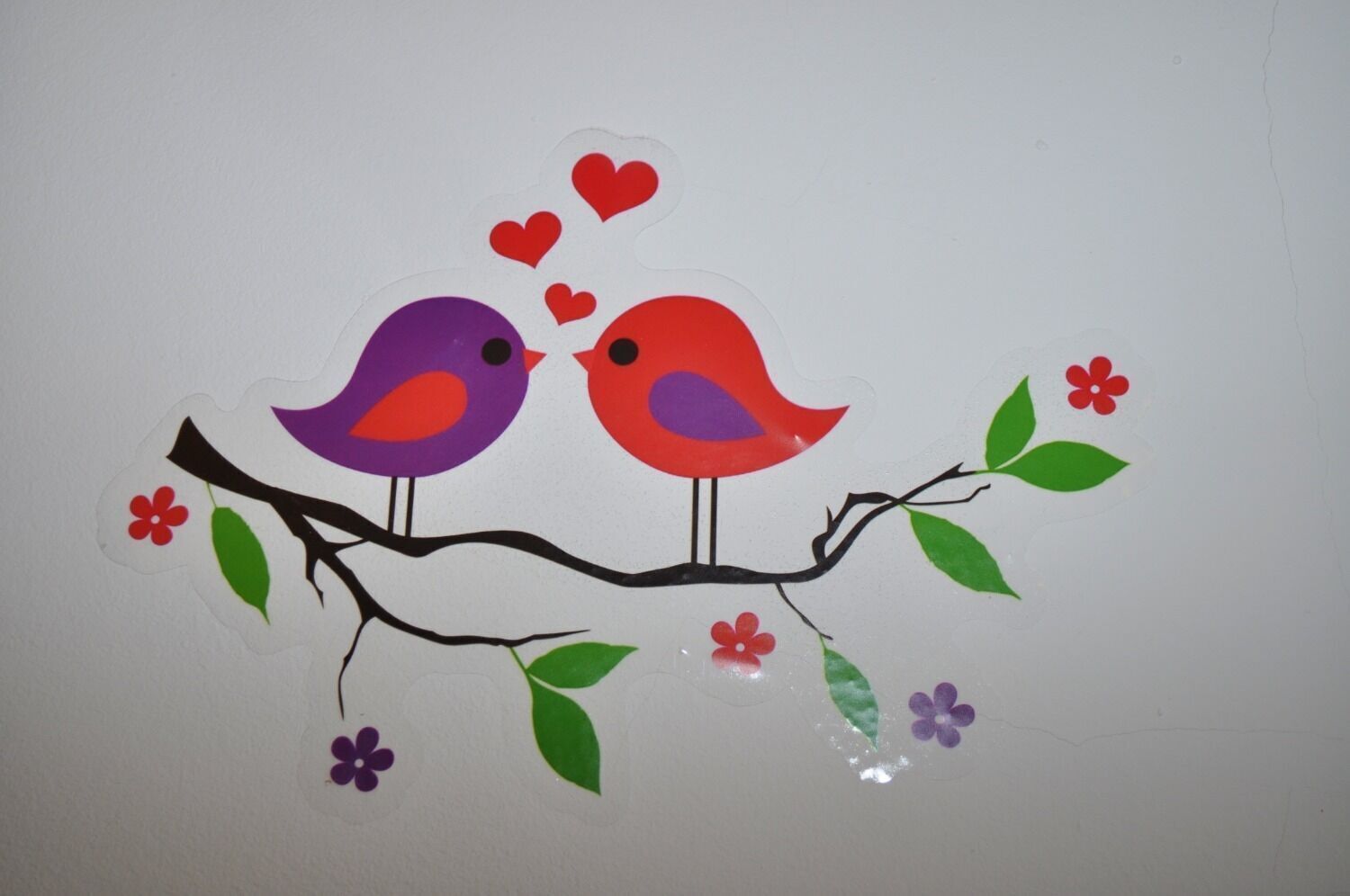 A decorative artwork of two birds on a branch with hearts and flowers.