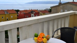 A balcony with a table and a wicker chair, overlooking a coastal town with red-roofed buildings and a view of the sea. - Apartments Ivi (Makarska)