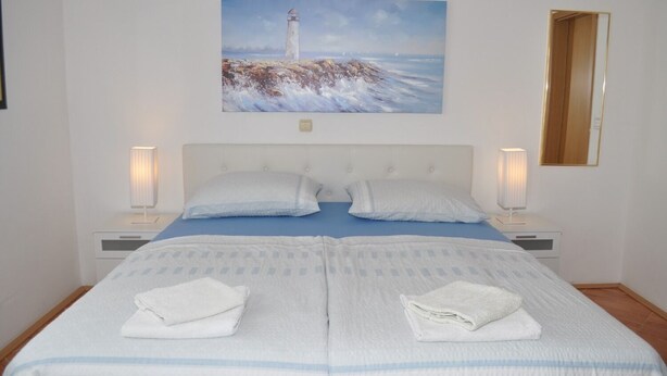 A bedroom with a bed, two bedside tables, a painting of a lighthouse, and a mirror on the wall. - Apartments Ivi (Makarska)