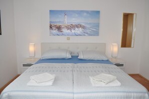 Een slaapkamer met een bed, twee nachtkastjes, een schilderij van een vuurtoren en een spiegel aan de muur.