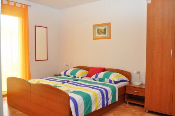 Une chambre à coucher comprenant un lit, une table de chevet, une armoire, un tableau encadré au mur et une fenêtre avec des rideaux.
