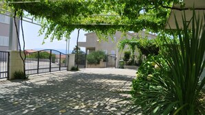 A paved courtyard with a metal gate, surrounded by greenery and buildings. - Apartments Ivi (Makarska)