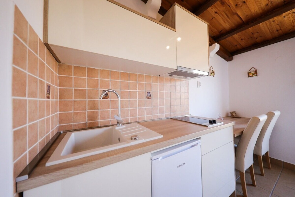 A kitchen with a sink, white cabinets, a dishwasher, and a wooden ceiling.
