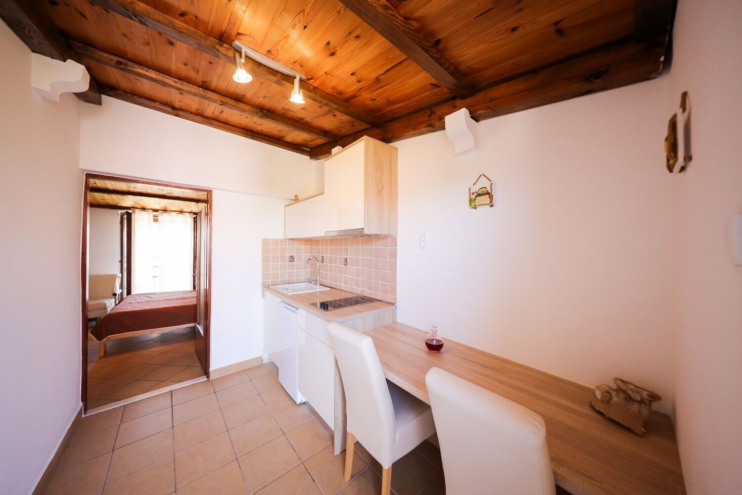A compact kitchen with a wooden ceiling, white tiles, a sink, and a dining area with chairs.