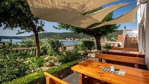 Une terrasse dotée de bancs en bois et d’une table, offrant une vue panoramique sur la côte, avec un ciel dégagé.