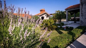 Une cour avec un bâtiment en pierre, un kiosque et des plants de lavande.