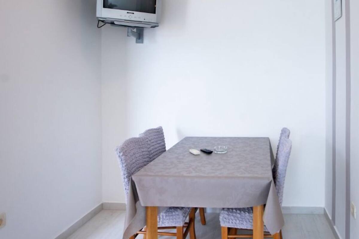 En matplats med ett bord och stolar, en väggmonterad tv och en lampa i taket.