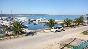 Una marina con barche ormeggiate, un'auto bianca parcheggiata a lato e un cielo azzurro limpido.