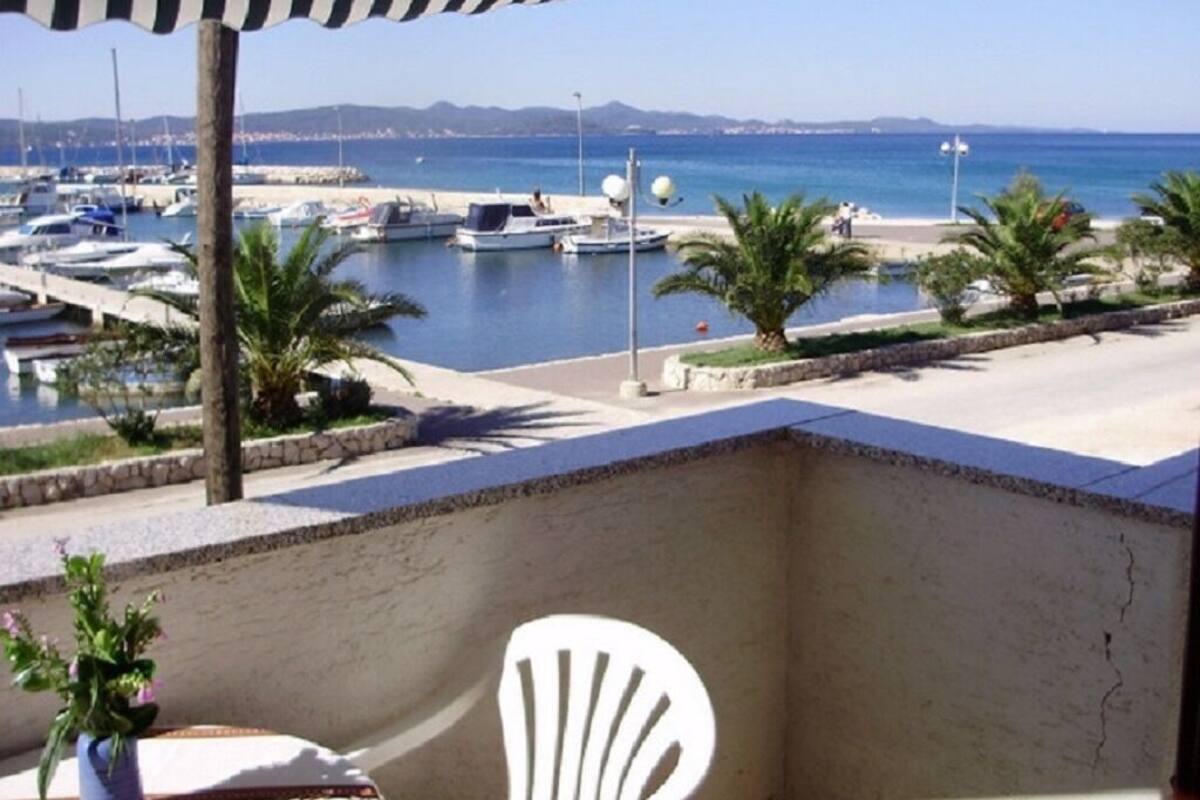 A balcony with a view of a marina, a white chair, and a potted plant.