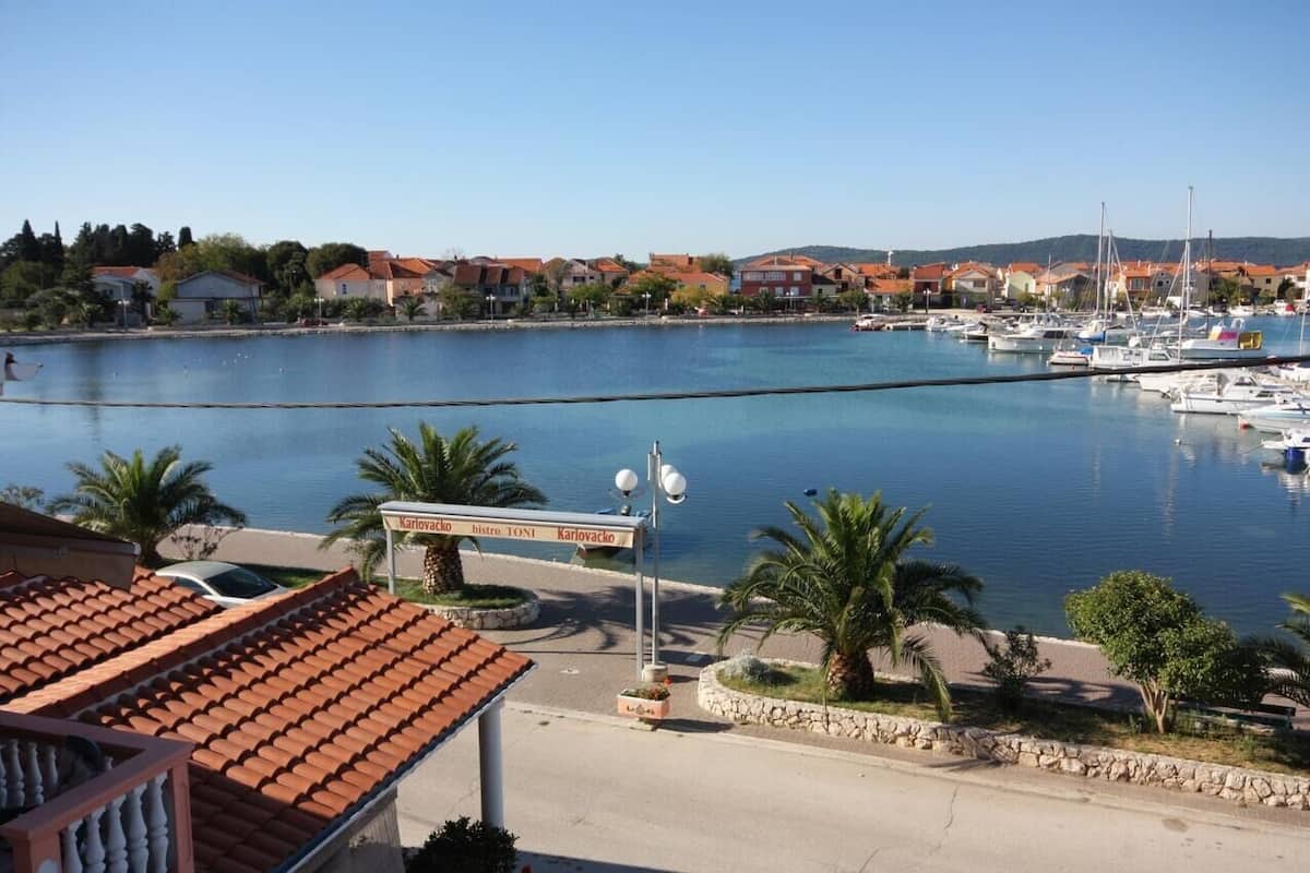 A marina with boats, a sign for 'Kariovac Bistro TONI', and a coastal residential area.
