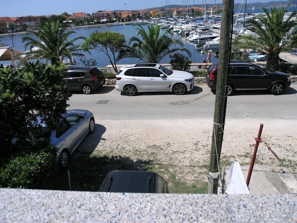 A marina with several parked cars and boats, surrounded by palm trees and buildings in the background.